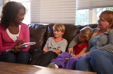 Woman Social Worker Speaking with Children and a Mother on a Couch