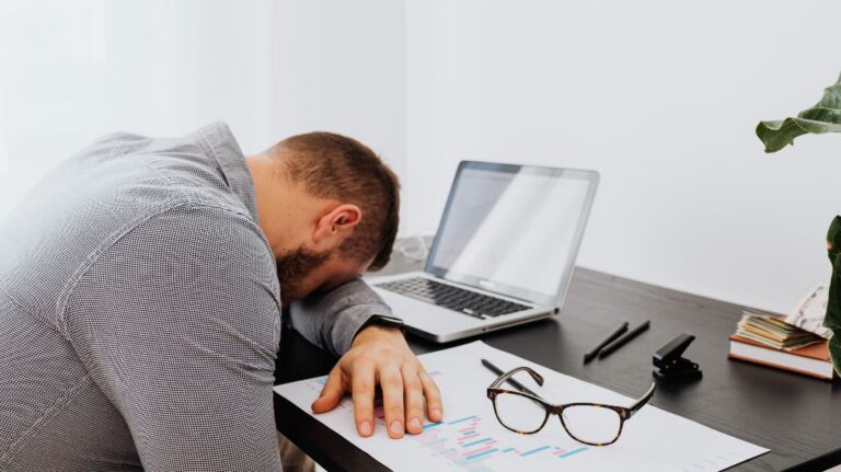 Exhausted Man with Head Down on Desk with Laptop