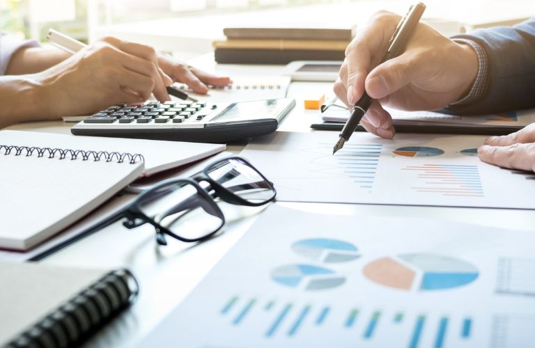 Stat Documents and Glasses on a Desk While Man and Woman Work